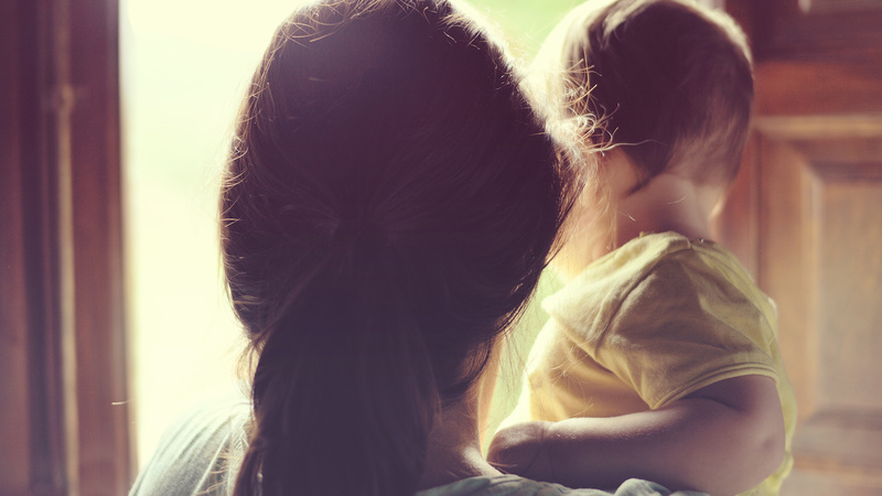 Family concept. Mother holding her little daughter next to the wooden window at sunset time. Backlit creates a candid ambient. / ©jdjuanci - stock.adobe.com, jdjuanci - stock.adobe.com